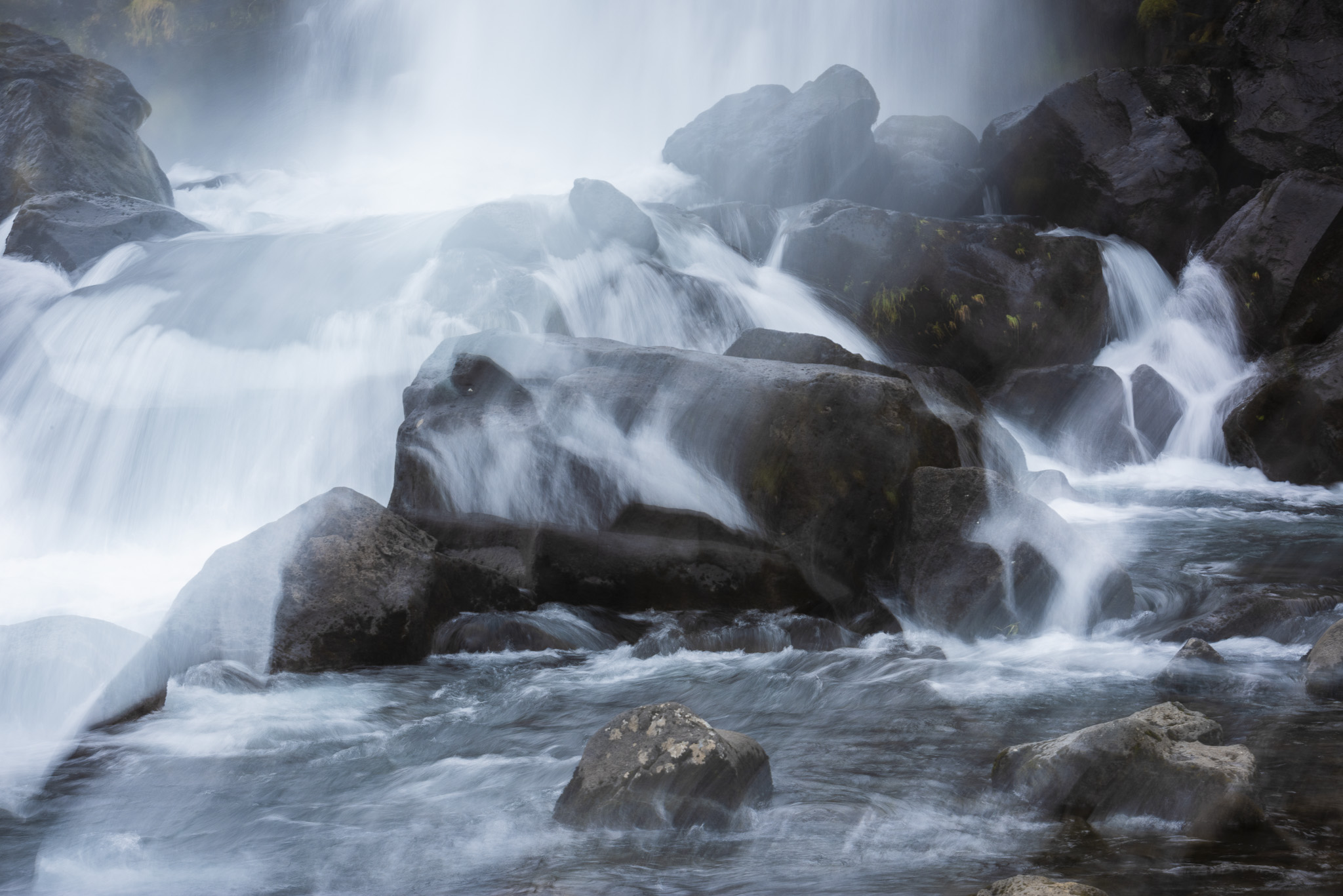 Abstraktes Bild mit dunklen Felsen sowie mit fließendem Wasser eines Wasserfalls.