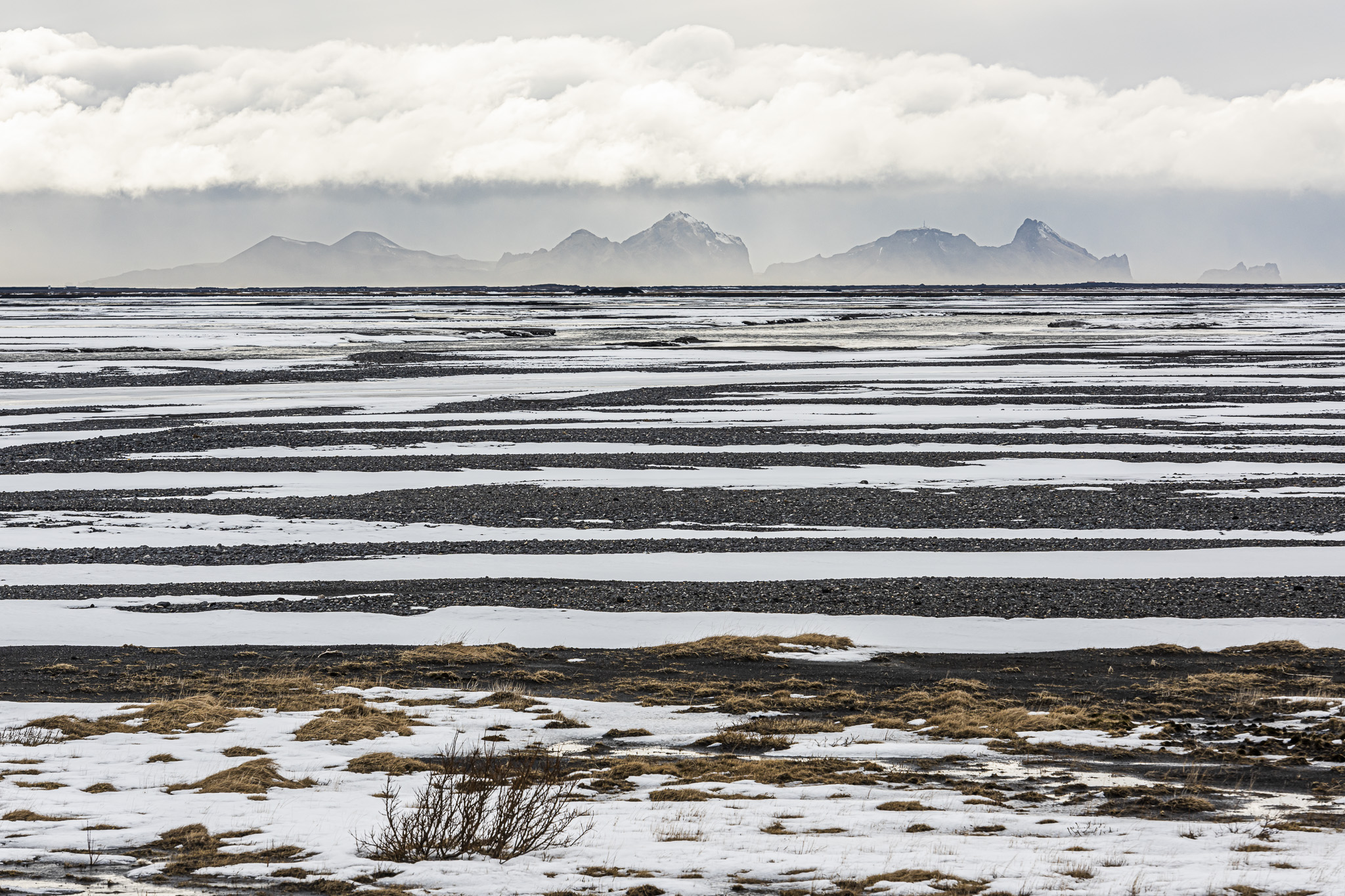 Flussdelta mit schwarz und weisse Strukturelemente mit Vestmannaeyjar am Horizont.