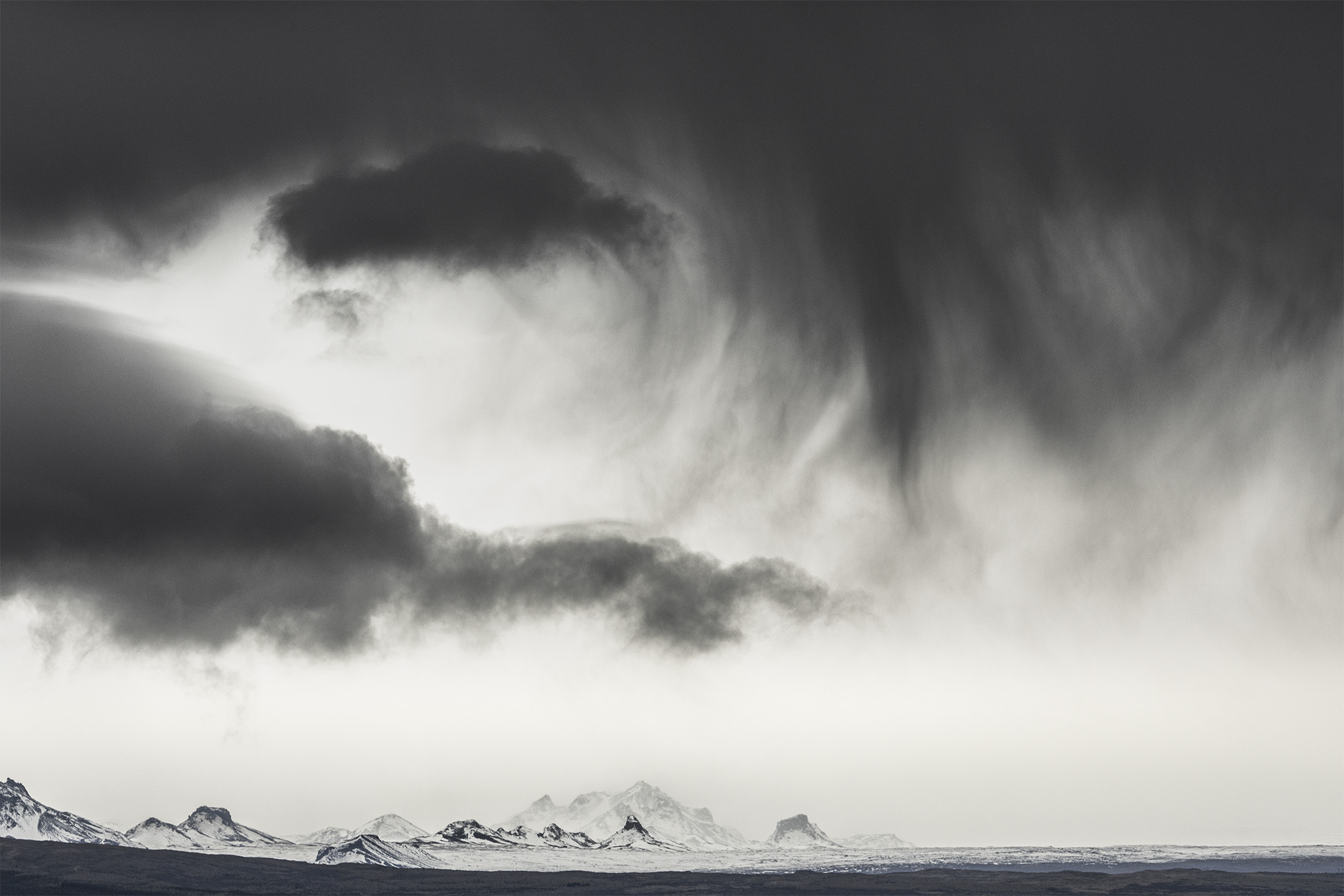 Landschaft in Island mit Bergen im Hintergrund uberragt von einigen dunklen Wolken, die Sturm andeuten.