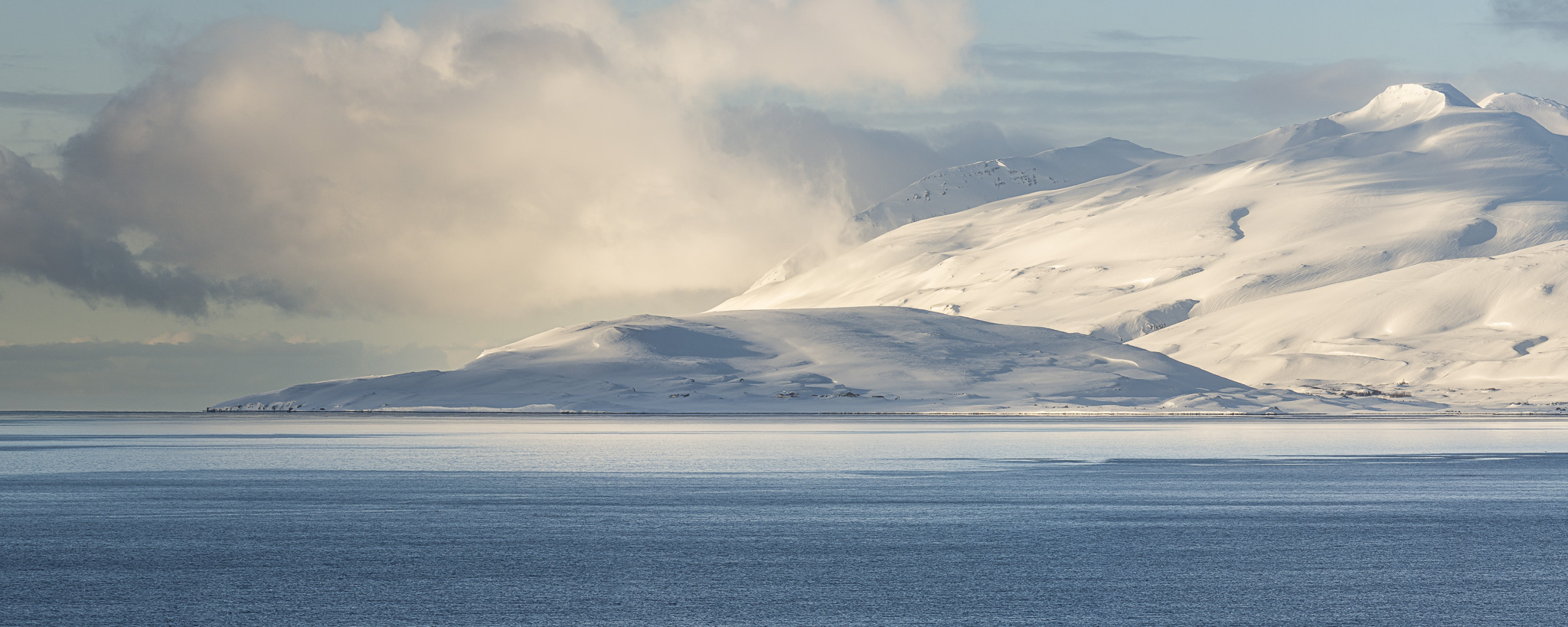 Panorama in Island einer Bucht mit schneebedeckten Bergen in blau und weiss.